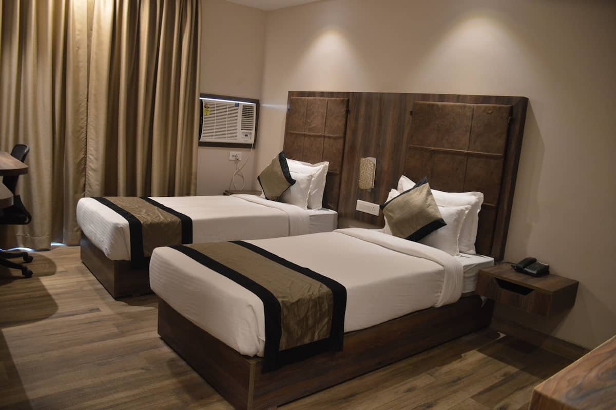 Quarto de hotel com duas camas de solteiro, cabeceira de madeira, mesa de cabeceira com telefone e escrivaninha com cadeira.