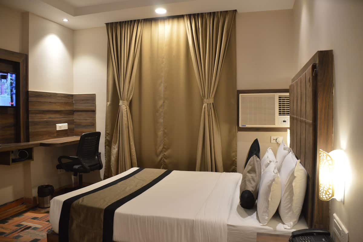 Quarto de hotel com cama, escrivaninha, cadeira, televisão e ar condicionado fixado na parede.