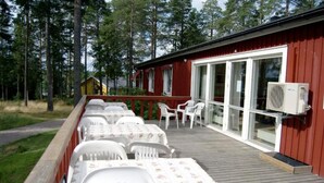 A wooden deck with white plastic chairs and tables, a red building with large windows, and a forested background. - Örnvik Hotell & Konferens (Luleå)