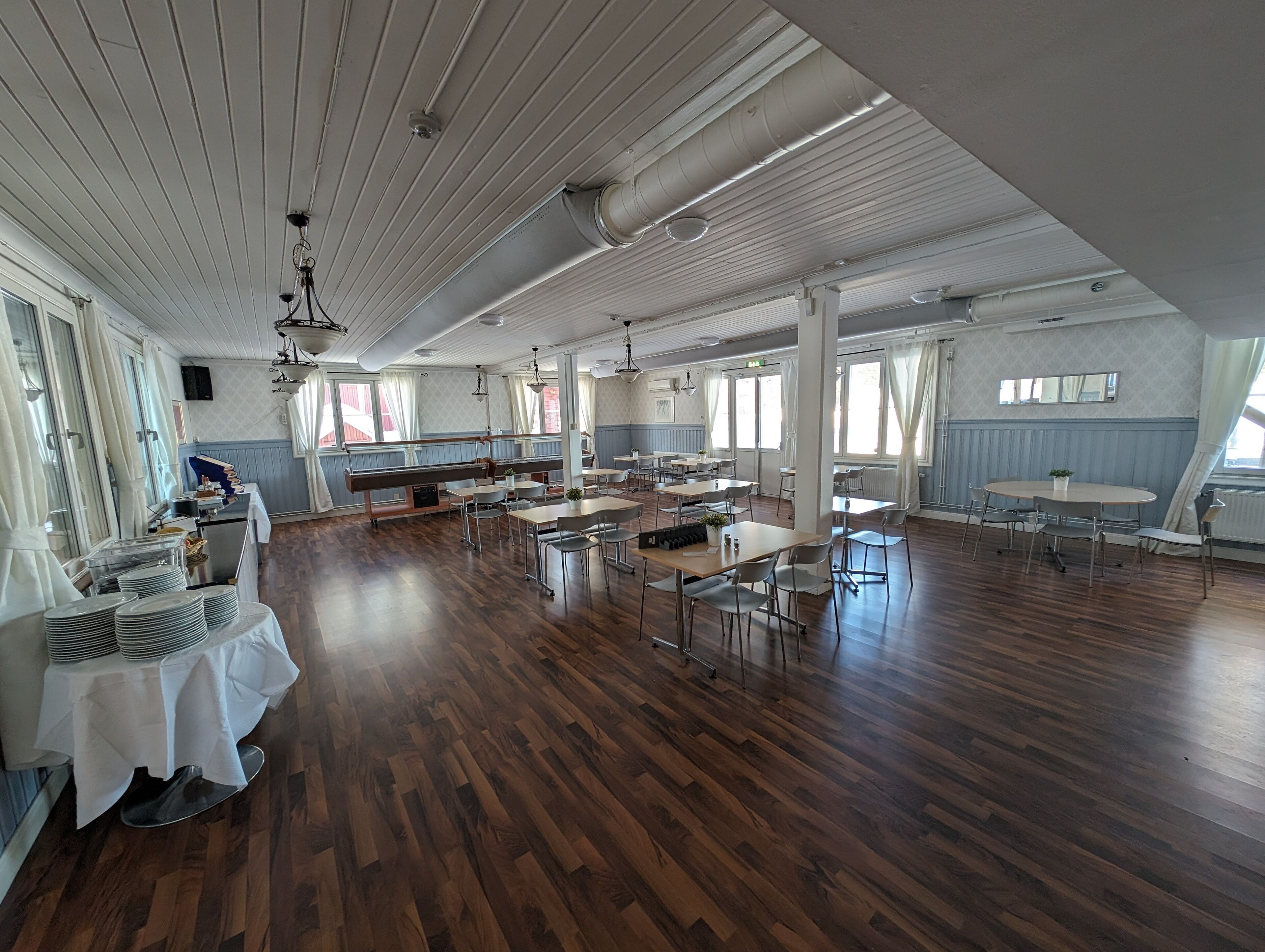 A spacious dining area with wooden floors, large windows, and a high ceiling with exposed beams.