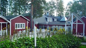 A red building with a covered outdoor area, surrounded by greenery and a bench. - Örnvik Hotell & Konferens (Luleå)