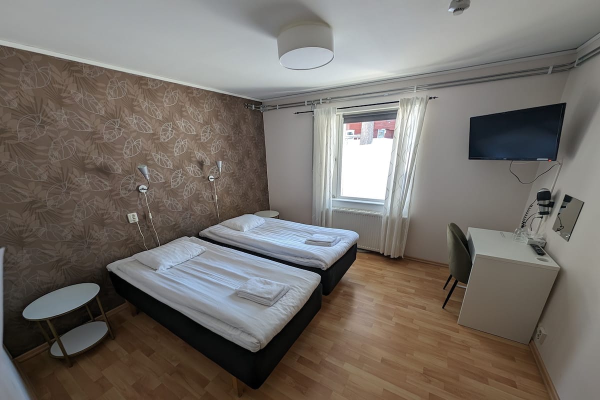 A hotel room with two beds, a desk, a TV, and a small table.