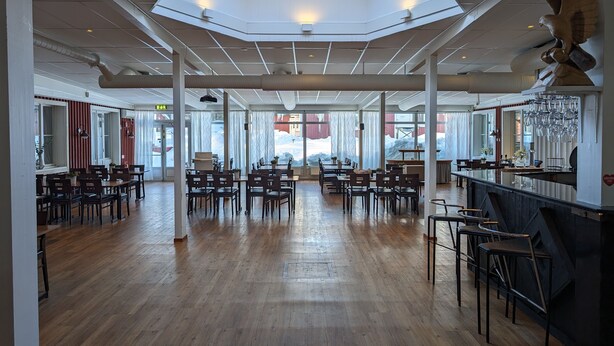 A spacious restaurant with high ceilings, wooden flooring, and large windows offering views of the snowy landscape. - Örnvik Hotell & Konferens (Luleå)