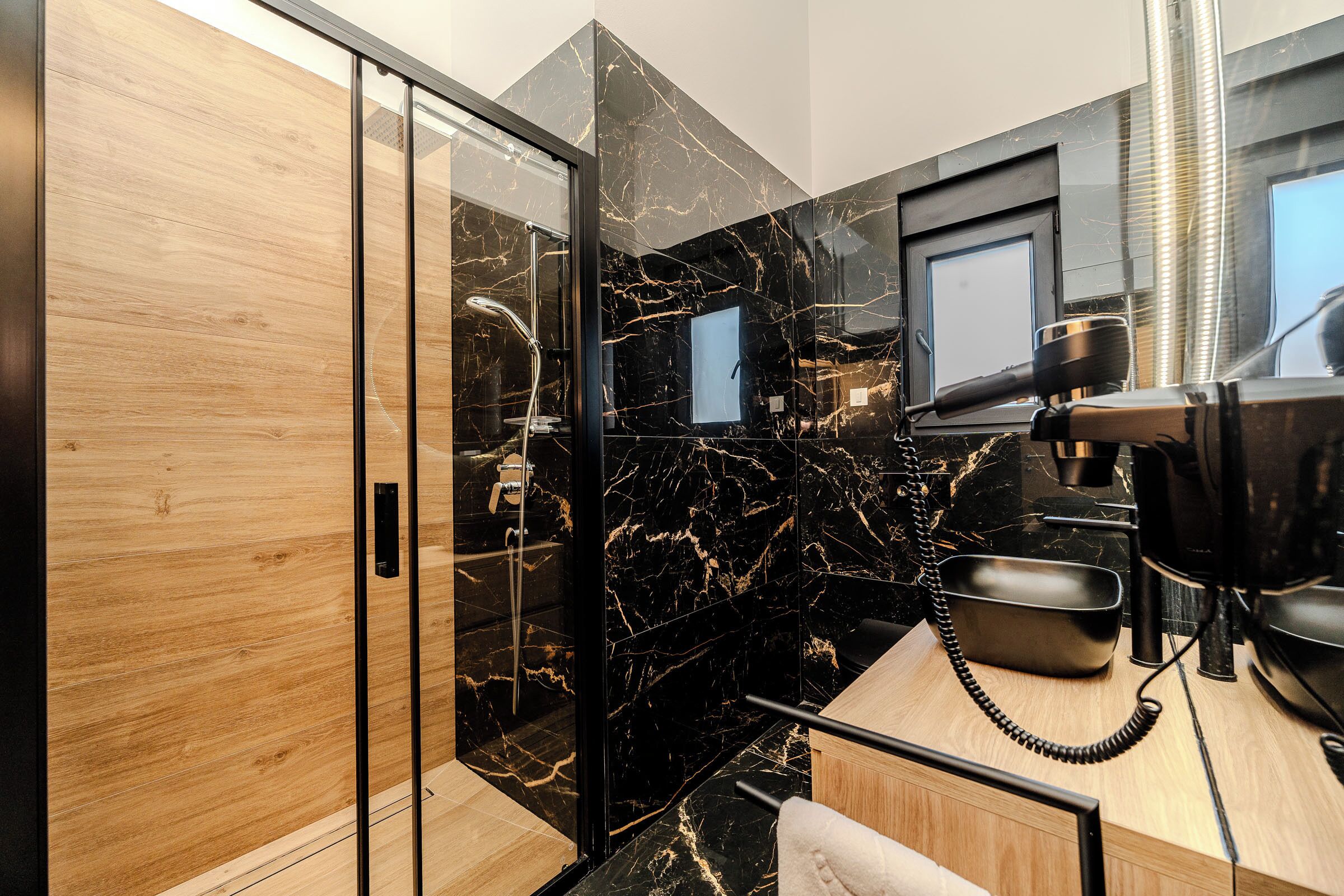 Un baño moderno con cabina de ducha de vidrio, tocador de madera y salpicadero de mármol.