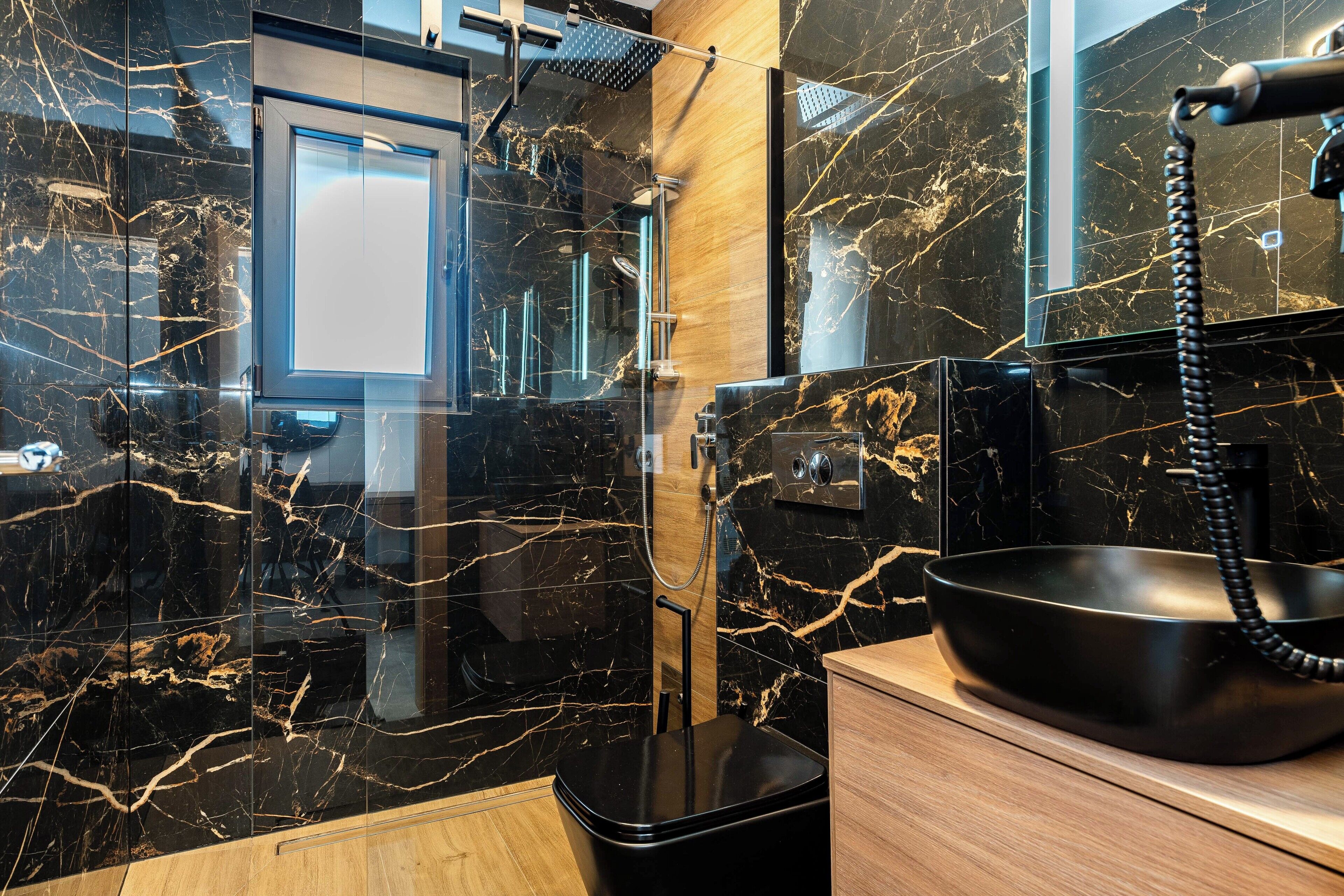 Un bagno moderno con un lavandino in marmo nero, un soffione a mano e un mobile bagno in legno.