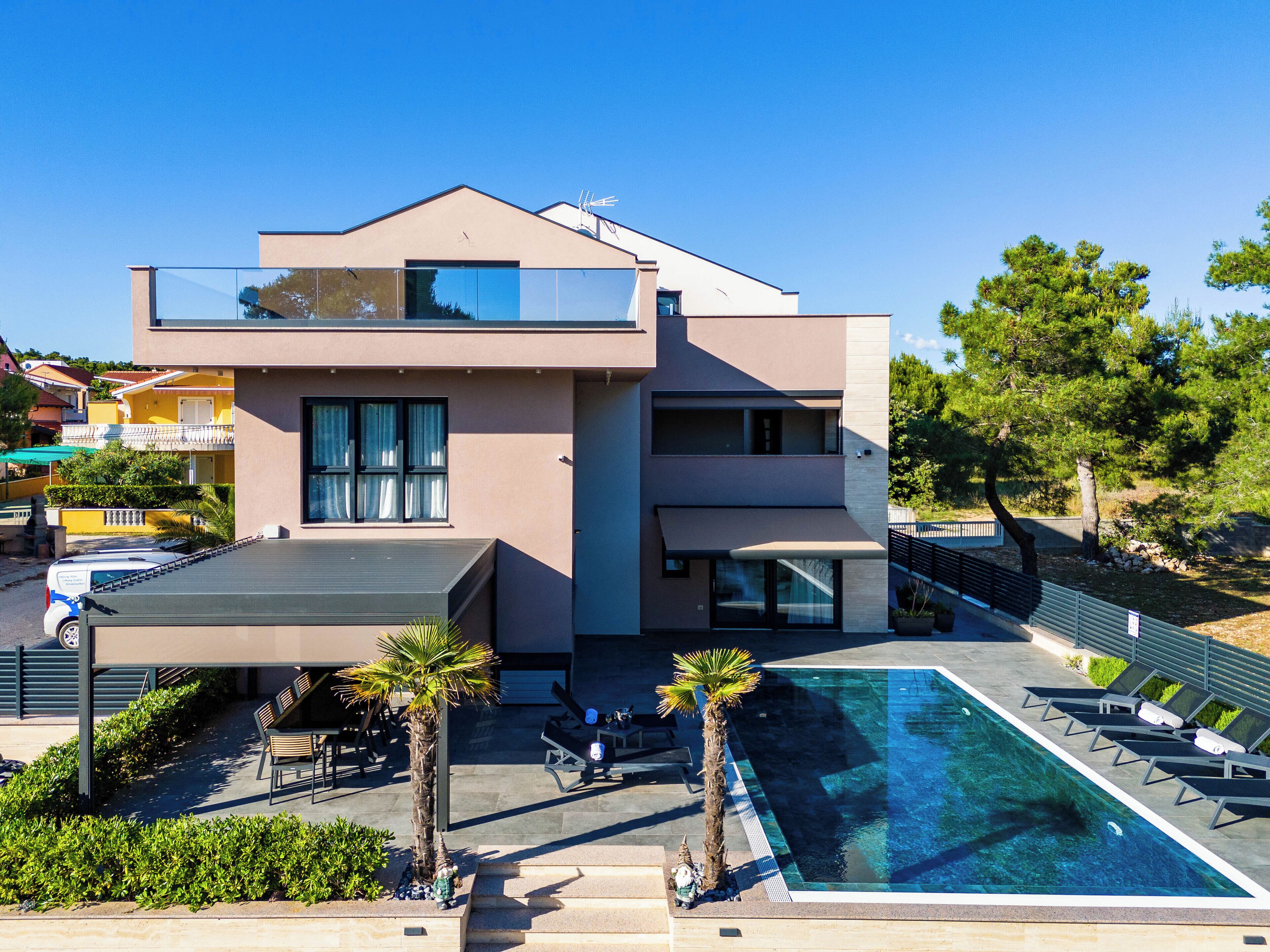 A modern two-story building with a rooftop terrace, a swimming pool, and outdoor seating.