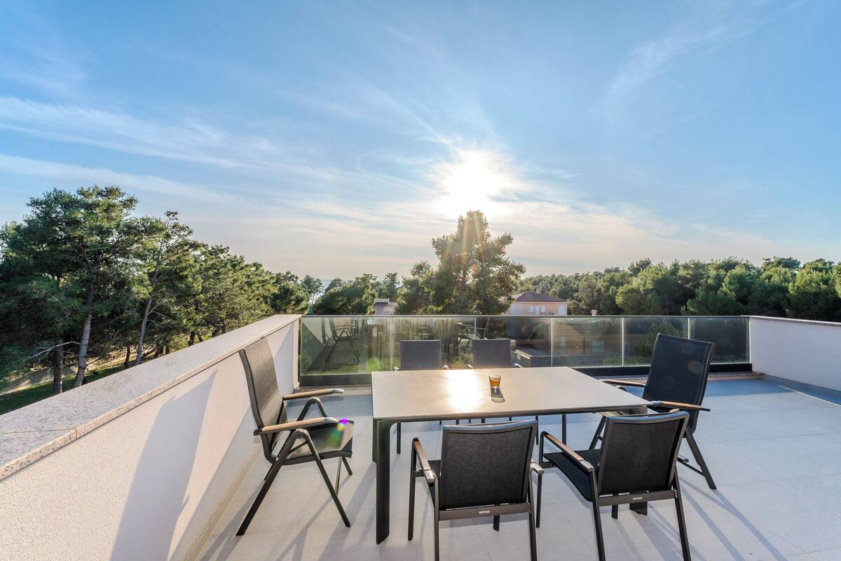 A rooftop terrace with a table and chairs, overlooking a cityscape and trees.