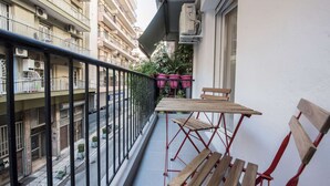 Een balkon met een houten tafel en stoelen, plantenbakken en uitzicht op een straat.