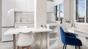 A modern kitchen with white cabinetry, a white countertop, and a blue chair. - Pearl: Penthouse suite with city view (Thessaloniki)