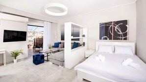 A modern hotel room with a bed, a seating area with a sofa and armchairs, a TV, and a large abstract painting. - Pearl: Penthouse suite with city view (Thessaloniki)