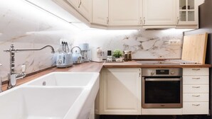 Une cuisine moderne avec des meubles blancs, un évier à deux bacs, un four encastré et un plan de travail en bois.