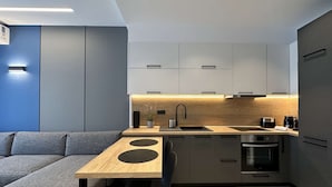 Una cocina moderna con encimera de madera, electrodomésticos integrados y un sofá gris en la sala de estar contigua.