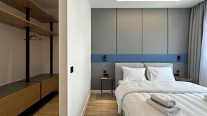 Una habitación de hotel moderna con una cama grande, mesitas de noche, un banco empotrado y un armario.