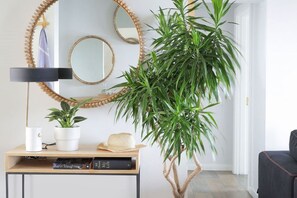 A room with a large potted plant, a mirror, a lamp, and a small table with books and a hat.