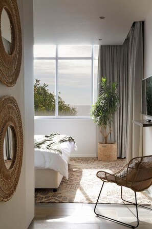 A modern bedroom with a large window, a bed, a chair, and a television. - Modern Clifton Apartment - Number 5101 (Cape Town)