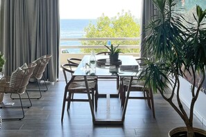 A dining area with a table and chairs, a potted plant, and a view of the sea. - Modern Clifton Apartment - Number 5101 (Cape Town)