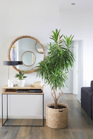 A modern living room with a wooden console table, a potted plant, a round mirror, and a dark sofa.