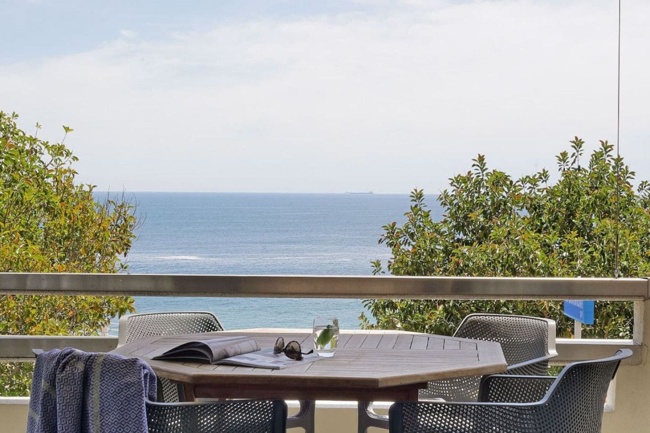 A balcony with a table and chairs overlooking the sea.