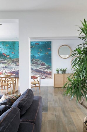 A living room with a large window, a sofa, a dining area, and a wooden cabinet.