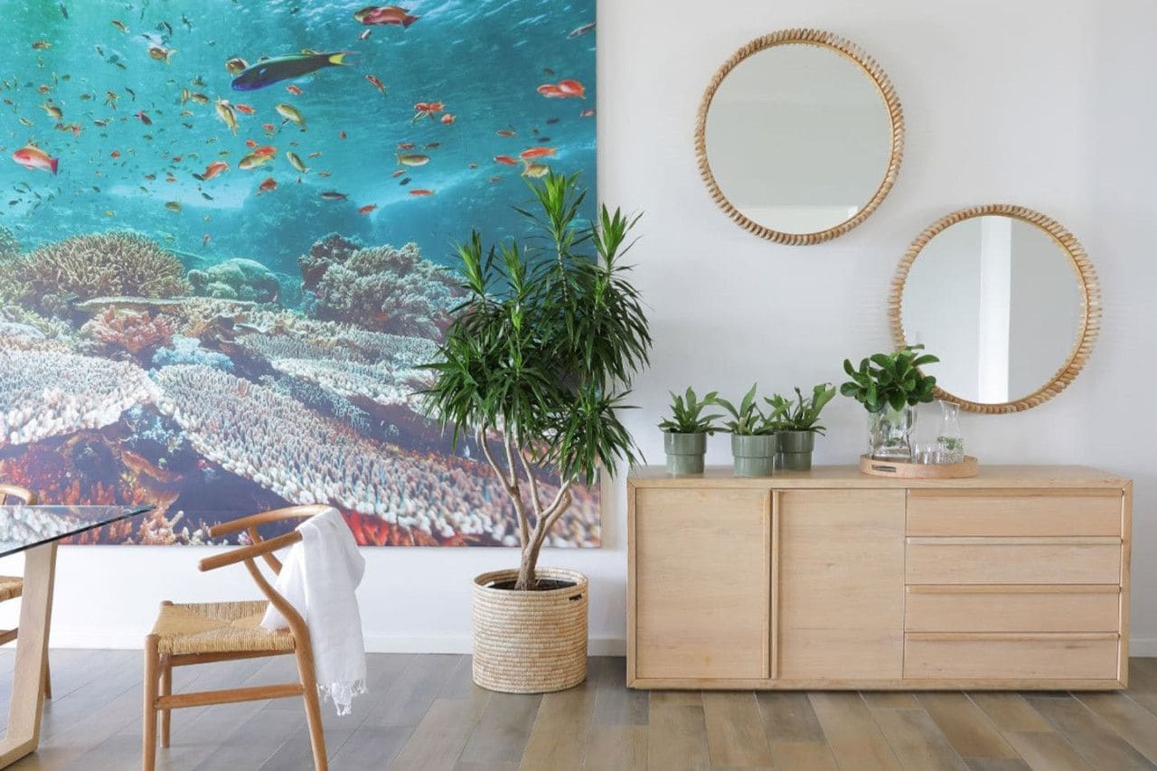 A room with a large wall mural of an underwater scene, a wooden cabinet with two mirrors, and a potted plant.