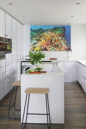 A modern kitchen with white cabinetry, a central island with stools, a sink, and a large painting above the island.