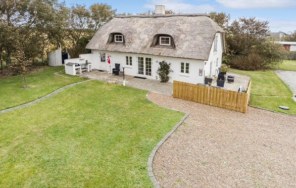 A thatched-roof house with a white exterior, a fenced yard, and a gravel driveway.