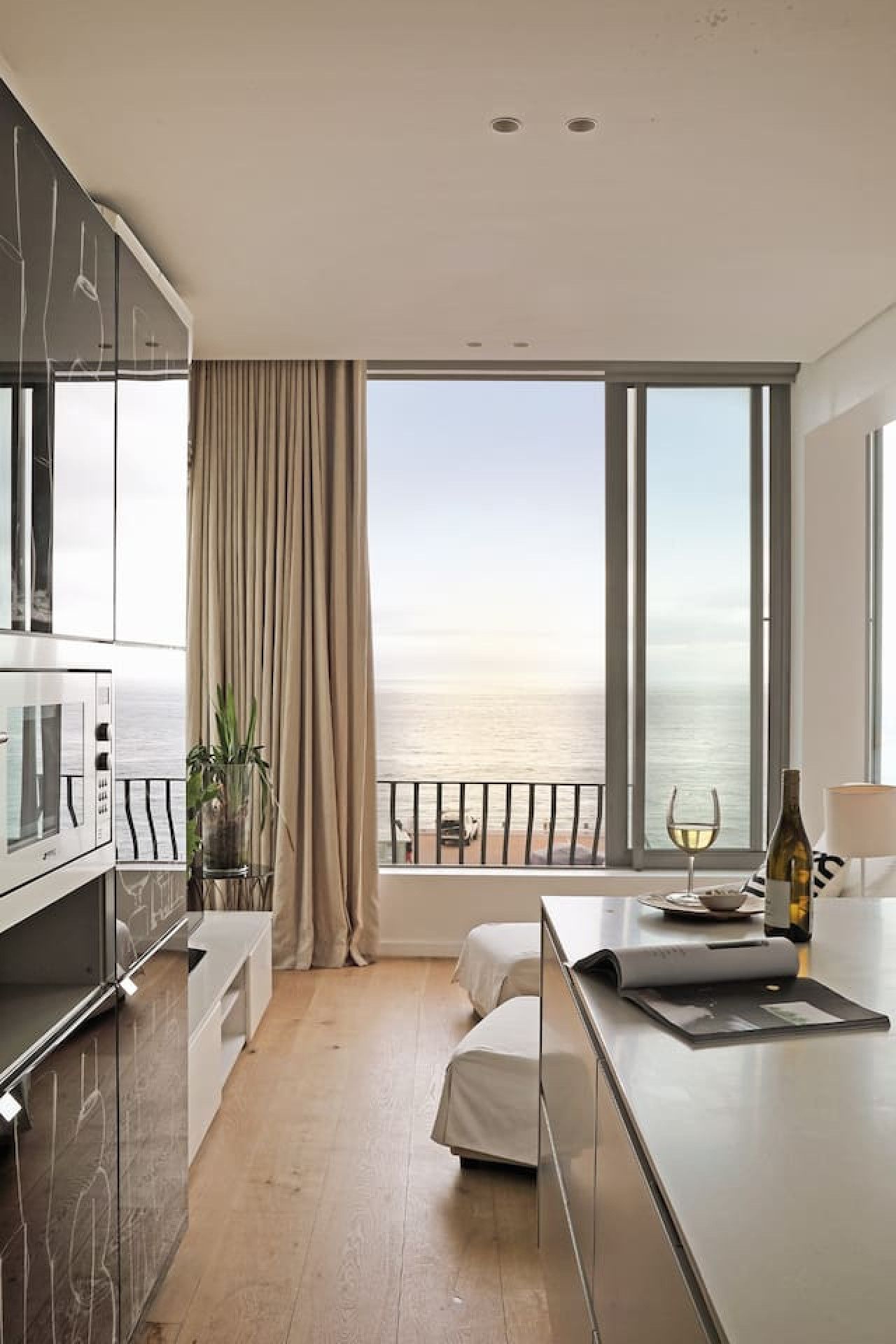 A modern kitchen with a large window, a dining area, and a view of the sea.