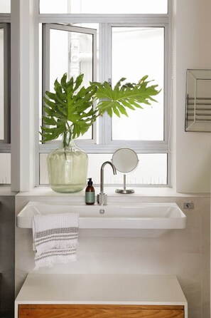 A bathroom with a white sink, a mirror, and a large green plant in a vase. - Unique Studio Apartment - Number 4704 (Cape Town)