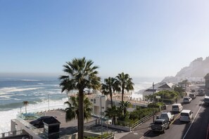 A coastal road with a view of the ocean, palm trees, and buildings. - Unique Studio Apartment - Number 4704 (Cape Town)