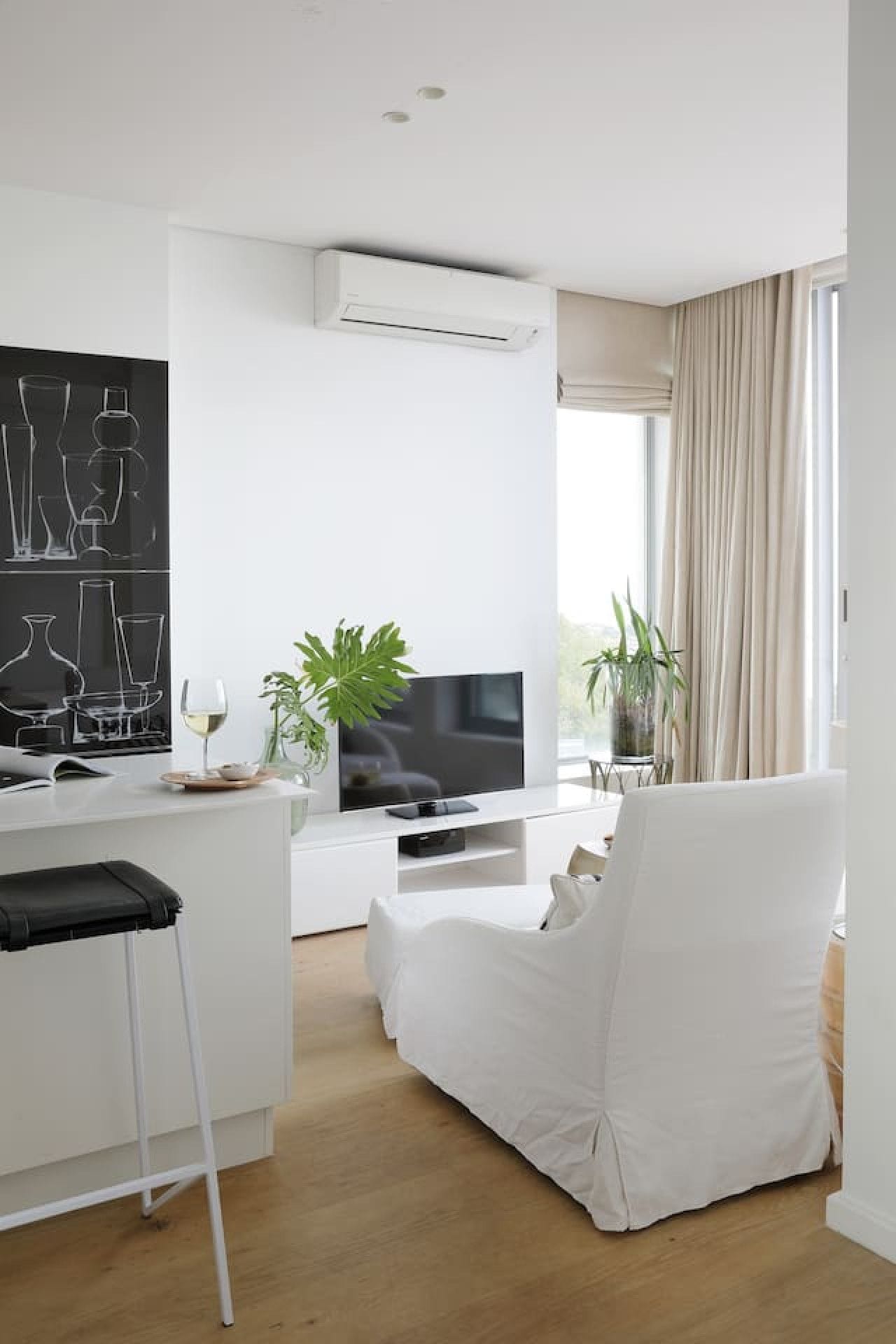 A modern living room with a flat-screen TV, a white sofa, and a dining area with a white table.