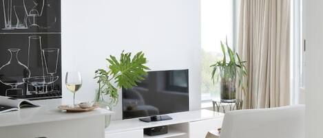 A modern living room with a flat-screen TV, a white sofa, and a dining area with a white table.
