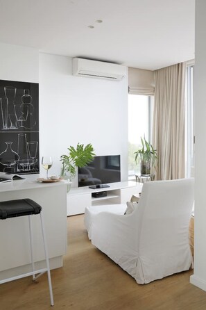 A modern living room with a flat-screen TV, a white sofa, and a dining area with a white table. - Unique Studio Apartment - Number 4704 (Cape Town)