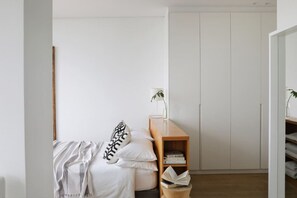 A bedroom with a bed, a bedside table with a lamp, a wooden bookshelf, and a wardrobe. - Unique Studio Apartment - Number 4704 (Cape Town)