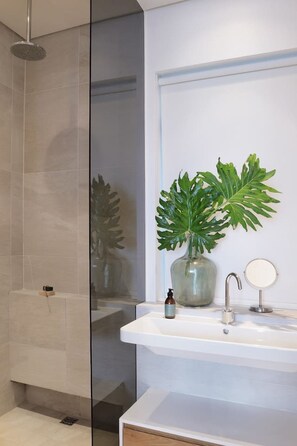 A modern bathroom with a glass shower enclosure, a white sink with a mirror, and a potted plant. - Unique Studio Apartment - Number 4704 (Cape Town)