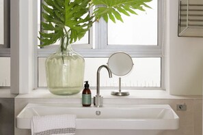 A bathroom with a white sink, a mirror, a bottle of soap, and a potted plant. - Unique Studio Apartment - Number 4704 (Cape Town)