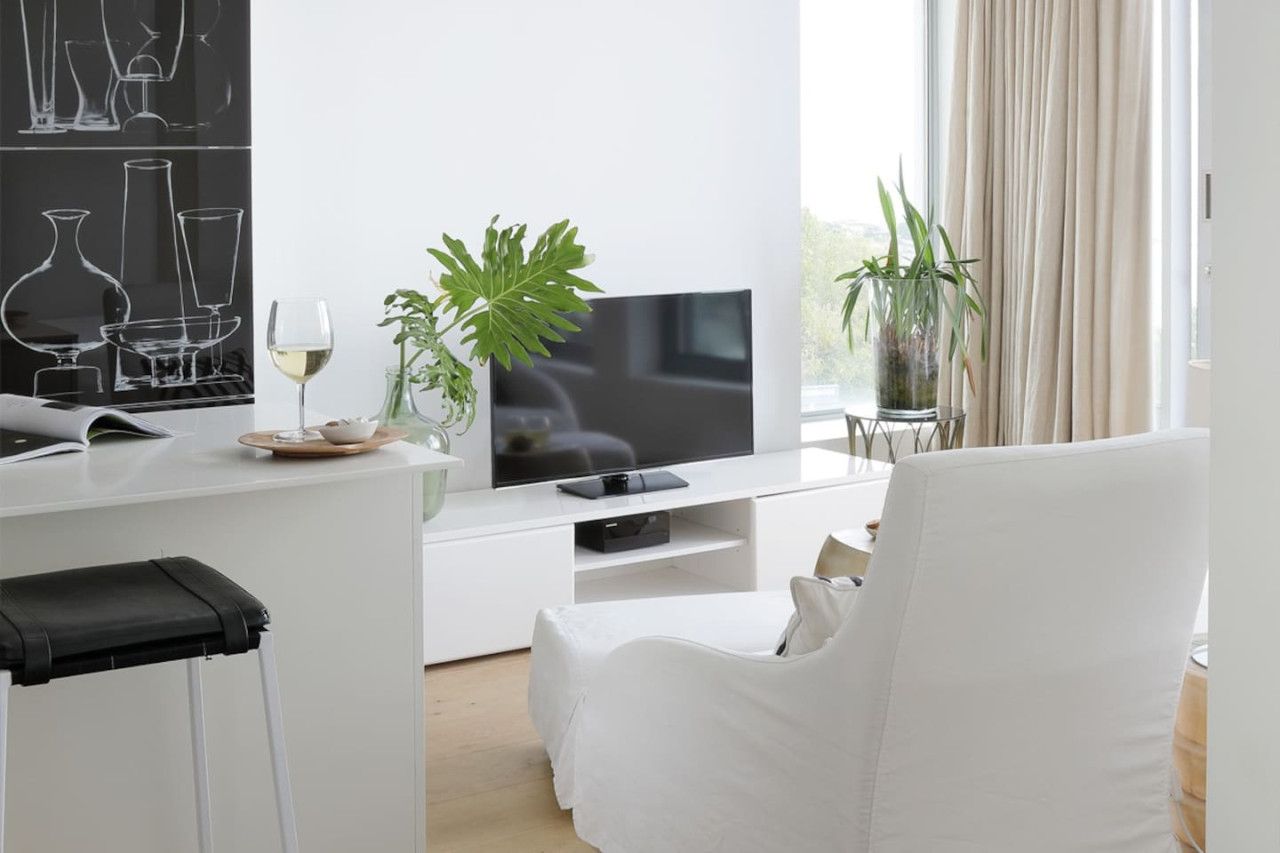 Una sala de estar moderna con un televisor de pantalla plana, muebles blancos y dos plantas en macetas.