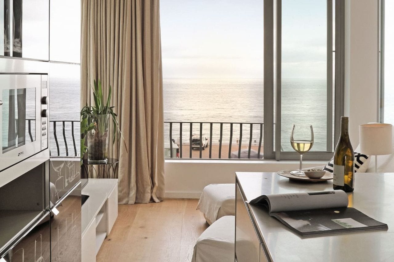 Une chambre d’hôtel avec vue sur la mer, une table à manger avec une bouteille de vin, et un téléviseur sur le côté gauche.