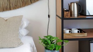 Une chambre à coucher moderne avec un lit, une lampe de chevet, une décoration murale en tissu tissé, une étagère avec des ustensiles de cuisine et une plante en pot.