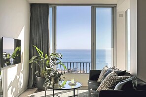 A balcony with a view of the sea, a sofa, a table with a drink, and a potted plant. - Spacious Studio Apartment - Number 4702 (Cape Town)