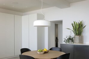 A modern dining area with a round table, black chairs, a white pendant light, and a potted plant on a cabinet. - Spacious Studio Apartment - Number 4702 (Cape Town)