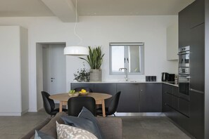 A modern kitchen with a dining area, featuring a central island, dark cabinetry, and stainless steel appliances. - Spacious Studio Apartment - Number 4702 (Cape Town)
