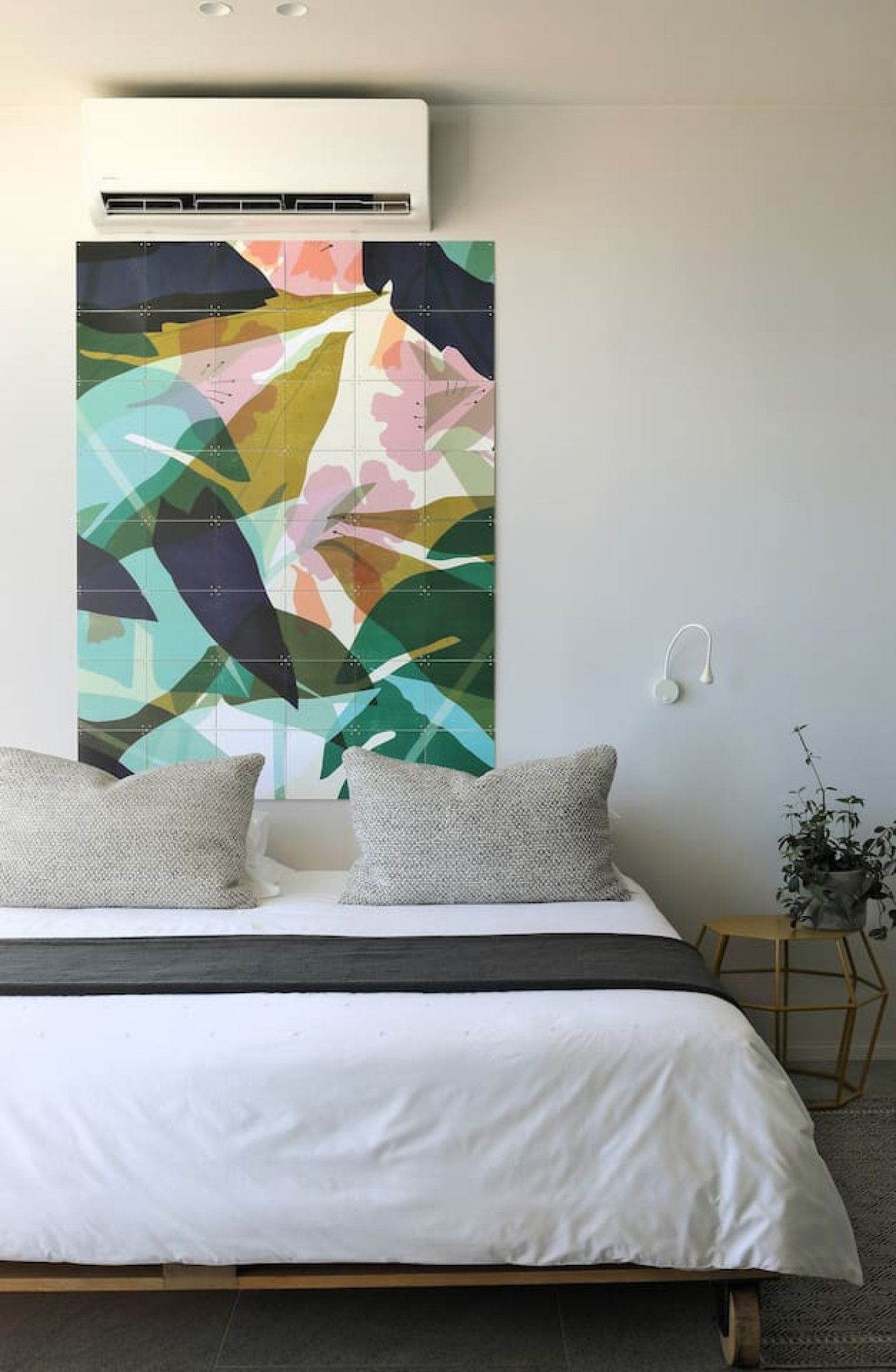 A modern bedroom with a large bed, a wall-mounted air conditioner, and a colorful abstract painting.