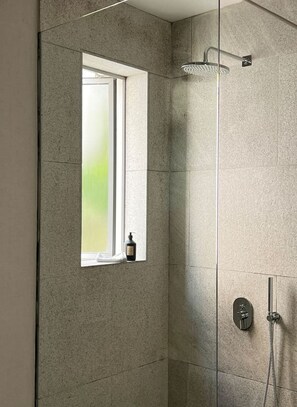 A shower with a window, a handheld showerhead, and a handheld faucet.