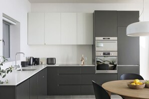 A modern kitchen with a central island, built-in appliances, and a dining area with a round table. - Spacious Studio Apartment - Number 4702 (Cape Town)