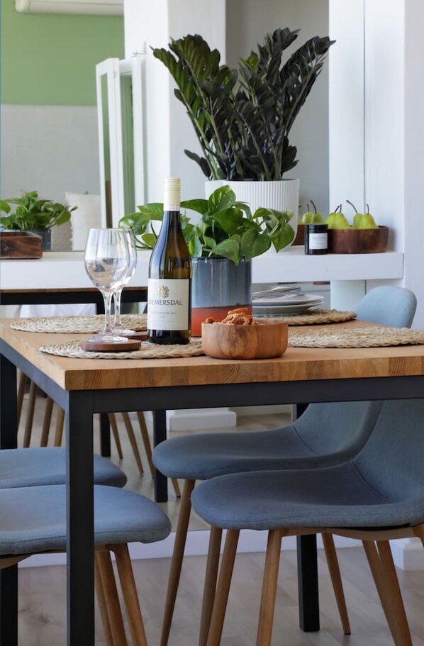 A dining table with a bottle of wine, a glass, and a bowl of food. There are chairs around the table.