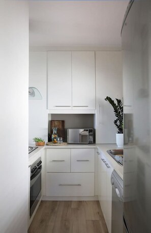 A compact kitchen with white cabinets, a microwave, a stove, and a dishwasher. - Cozy Studio Apartment - Number 4705 (Cape Town)