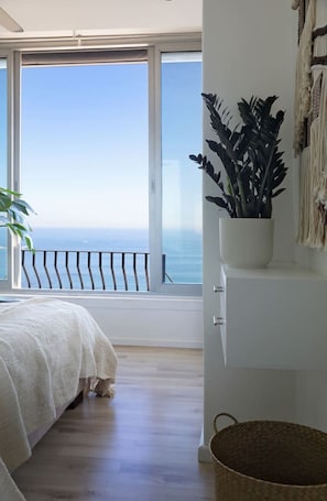 A bedroom with a large window, a bed, a potted plant, and a white cabinet. - Cozy Studio Apartment - Number 4705 (Cape Town)