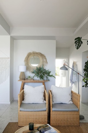 Ein Zimmer mit zwei Korbstühlen, einem runden Spiegel, einer Lampe und einer Blumentopf-Pflanze.