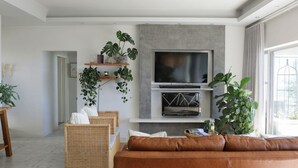 A modern living room with a flat-screen TV, wicker furniture, and potted plants. - Comfortable 3 Bedroom Apartment - Number 5103 (Cape Town)