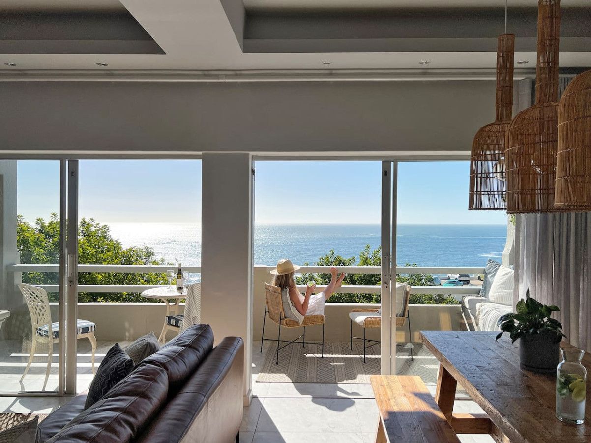 A modern living room with a large glass door leading to a balcony overlooking the sea.